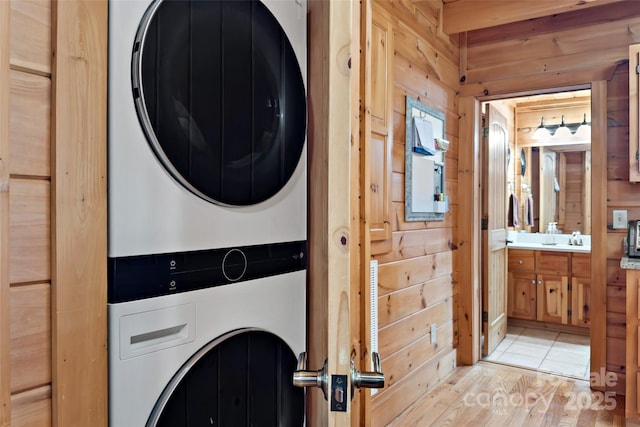 laundry room featuring stacked washer and dryer, laundry area, light wood-style flooring, wood walls, and a sink