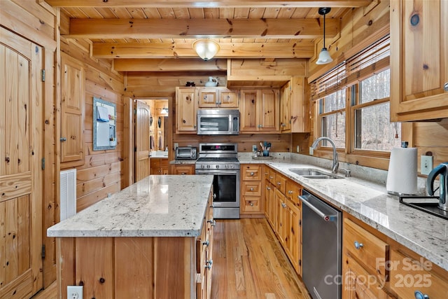 kitchen with light stone counters, a sink, appliances with stainless steel finishes, a center island, and decorative light fixtures