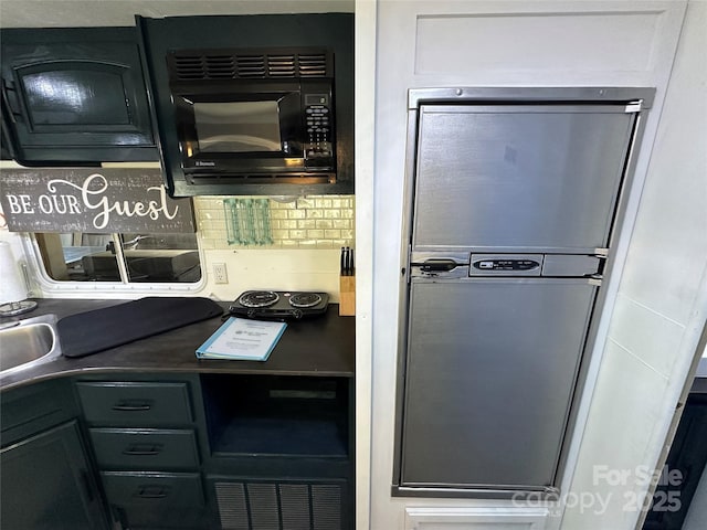 kitchen with black microwave, backsplash, dark countertops, and stainless steel fridge