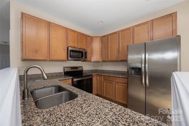 kitchen featuring brown cabinetry, dark stone counters, stainless steel appliances, a sink, and recessed lighting