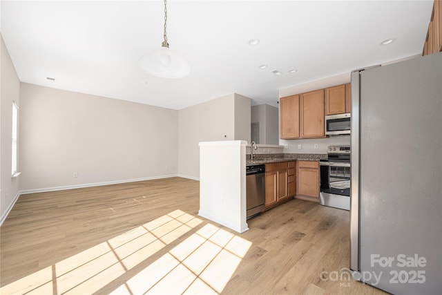 kitchen with pendant lighting, light wood-style flooring, appliances with stainless steel finishes, a sink, and baseboards