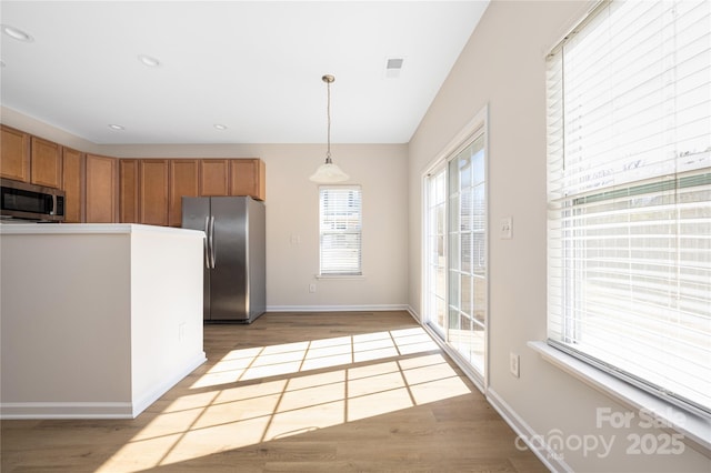 kitchen with light wood-style flooring, appliances with stainless steel finishes, brown cabinets, and decorative light fixtures