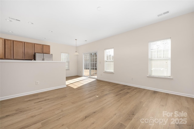 unfurnished living room with light wood finished floors, visible vents, and baseboards