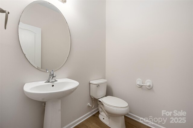 half bathroom with baseboards, toilet, and wood finished floors