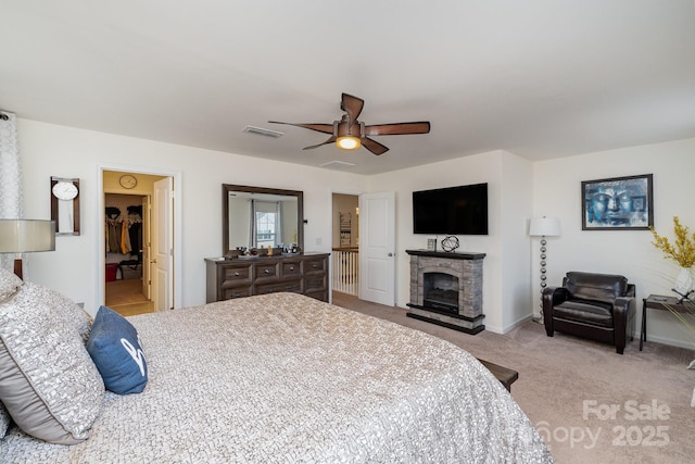 carpeted bedroom featuring ceiling fan, a fireplace, visible vents, baseboards, and a walk in closet