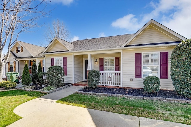 ranch-style house featuring a shingled roof, a front yard, and covered porch