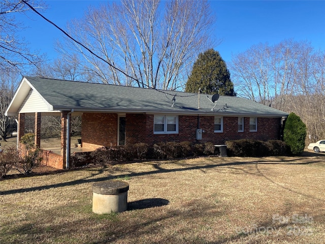 rear view of house featuring roof with shingles, brick siding, a lawn, and central air condition unit