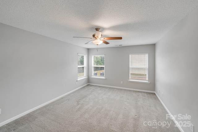 unfurnished room featuring light colored carpet, visible vents, ceiling fan, a textured ceiling, and baseboards