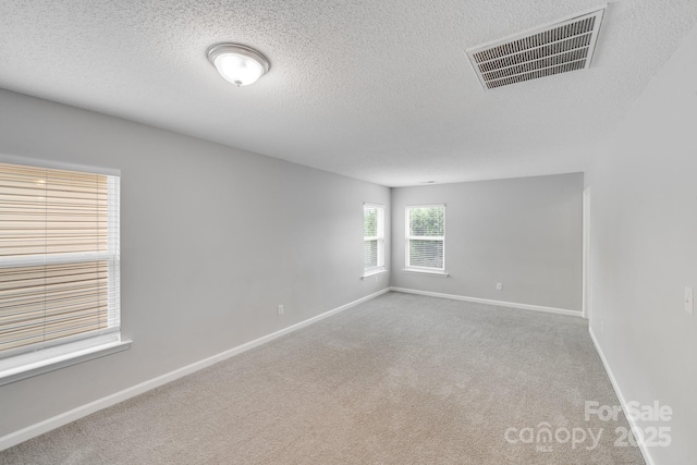 unfurnished room featuring a textured ceiling, carpet floors, visible vents, and baseboards