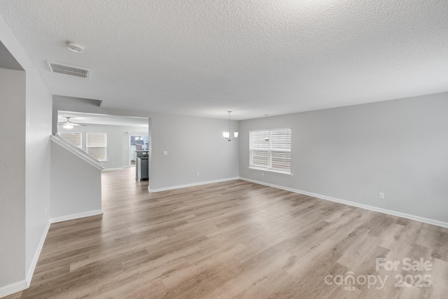 unfurnished living room featuring light wood finished floors, baseboards, visible vents, a textured ceiling, and ceiling fan with notable chandelier