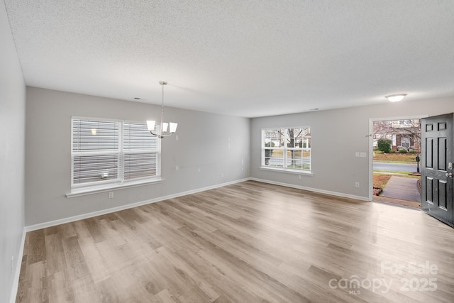 unfurnished dining area featuring an inviting chandelier, light wood-style flooring, baseboards, and a textured ceiling