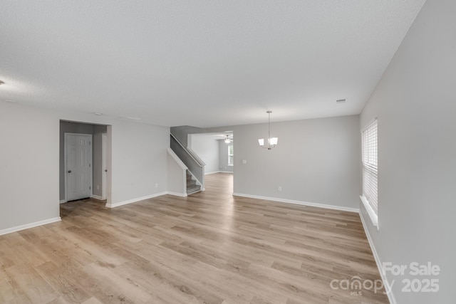 unfurnished living room with a textured ceiling, visible vents, baseboards, stairs, and light wood-type flooring