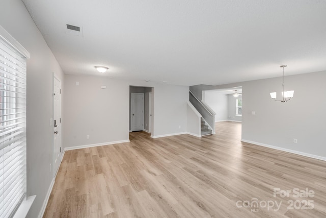 unfurnished living room with light wood finished floors, baseboards, stairway, and ceiling fan with notable chandelier