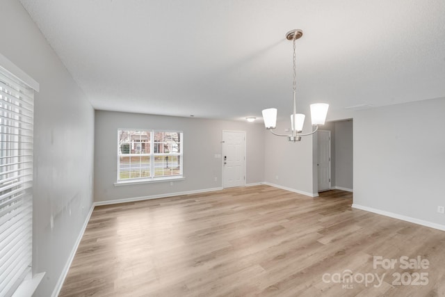 empty room featuring a chandelier, baseboards, and light wood-style floors