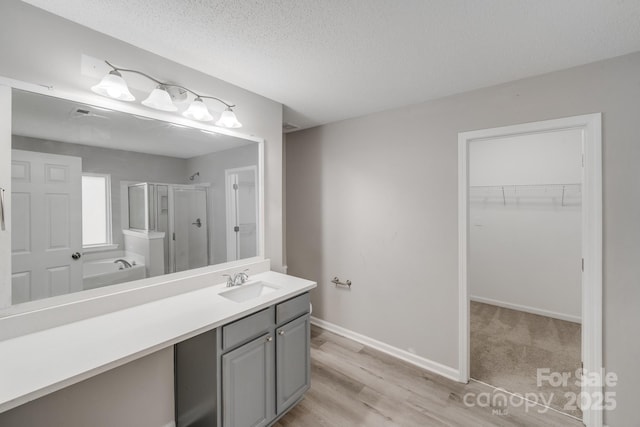 bathroom with a walk in closet, a stall shower, vanity, a textured ceiling, and baseboards