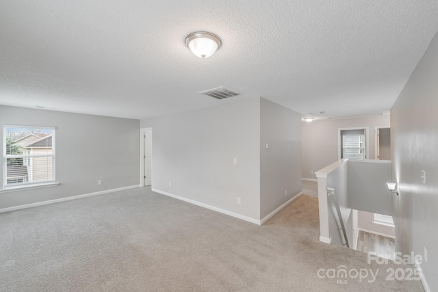 empty room with visible vents, light carpet, baseboards, and a textured ceiling