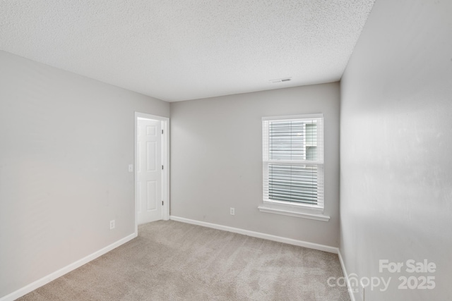 spare room with light carpet, visible vents, baseboards, and a textured ceiling