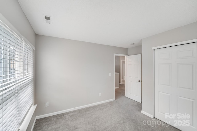 unfurnished bedroom featuring light colored carpet, a closet, visible vents, and baseboards