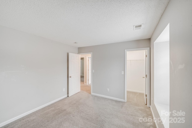 unfurnished bedroom with a walk in closet, visible vents, light carpet, a textured ceiling, and baseboards