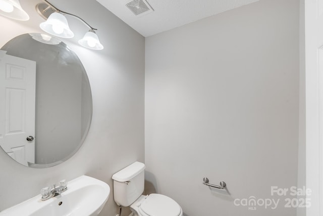 bathroom featuring toilet, a sink, and visible vents