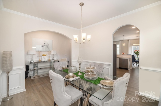 dining area featuring a decorative wall, wainscoting, wood finished floors, and crown molding