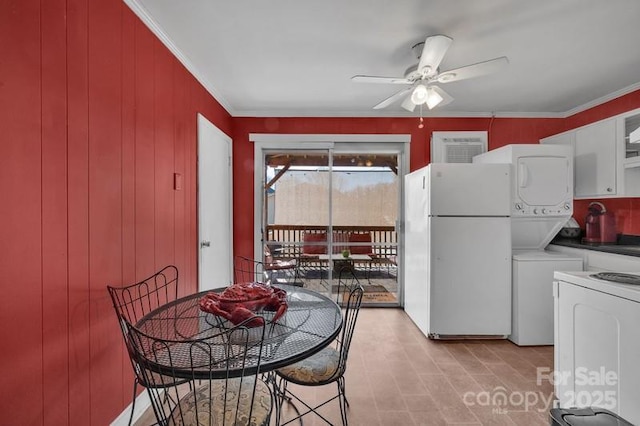 dining area with a ceiling fan, stacked washer / drying machine, crown molding, and wooden walls