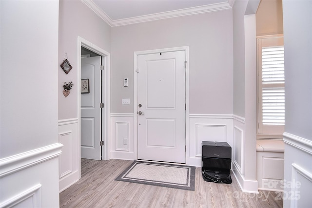 foyer entrance featuring ornamental molding, a decorative wall, wood finished floors, and wainscoting