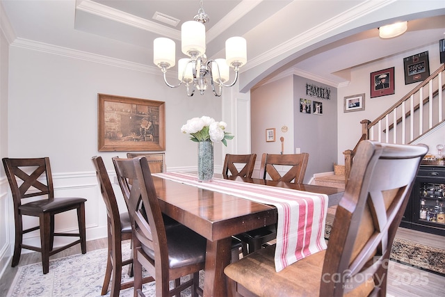 dining area with ornamental molding, arched walkways, wainscoting, and light wood-style flooring