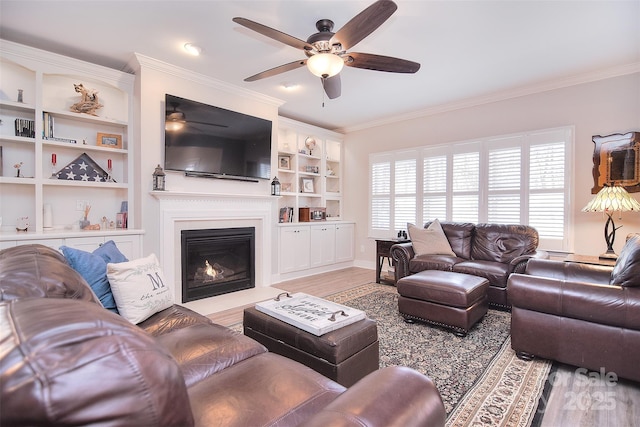 living room featuring a ceiling fan, a fireplace with flush hearth, light wood-style flooring, and crown molding