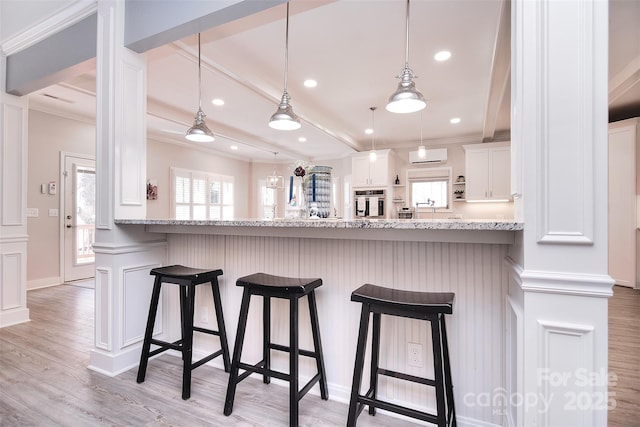 kitchen featuring light wood-style flooring, ornamental molding, a kitchen breakfast bar, white cabinetry, and beam ceiling