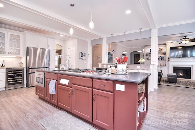 kitchen featuring a warm lit fireplace, wine cooler, open floor plan, appliances with stainless steel finishes, and light wood-type flooring