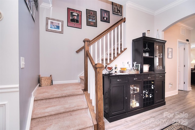 stairs featuring baseboards, arched walkways, crown molding, and wood finished floors