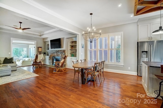 dining room featuring built in features, baseboards, wood finished floors, crown molding, and a fireplace