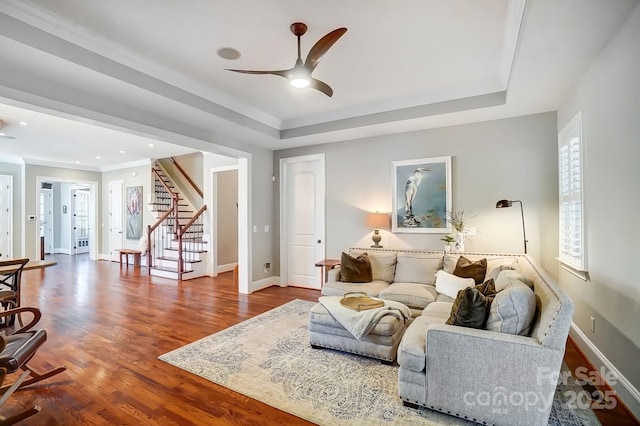 living area with wood finished floors, a raised ceiling, baseboards, and stairs