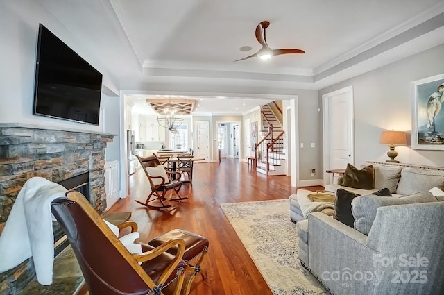 living room featuring a tray ceiling, stairway, wood finished floors, and crown molding