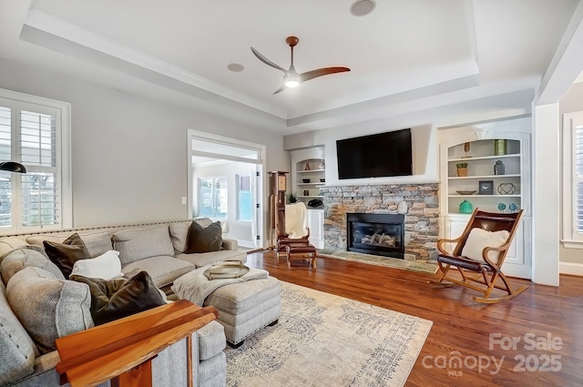 living area with wood finished floors, a fireplace, and a raised ceiling