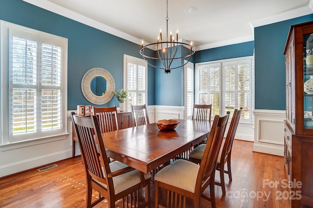 dining area featuring a wainscoted wall, visible vents, wood finished floors, and ornamental molding