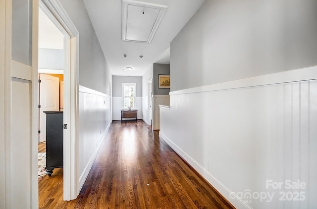 hall with a wainscoted wall, attic access, and dark wood-style flooring