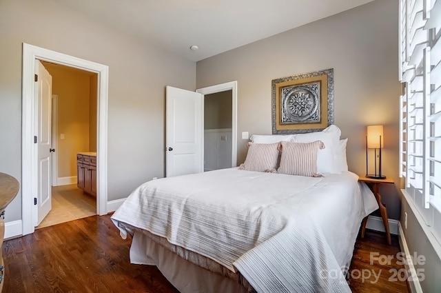 bedroom with connected bathroom, baseboards, and wood finished floors