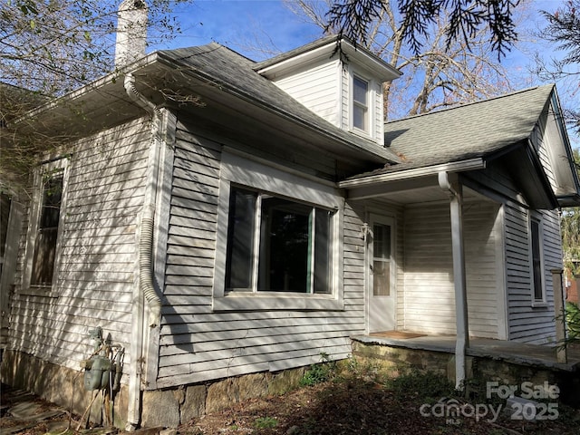 view of side of home with a shingled roof, crawl space, and a chimney