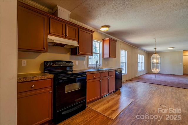 kitchen featuring under cabinet range hood, light wood-type flooring, black appliances, dark countertops, and crown molding