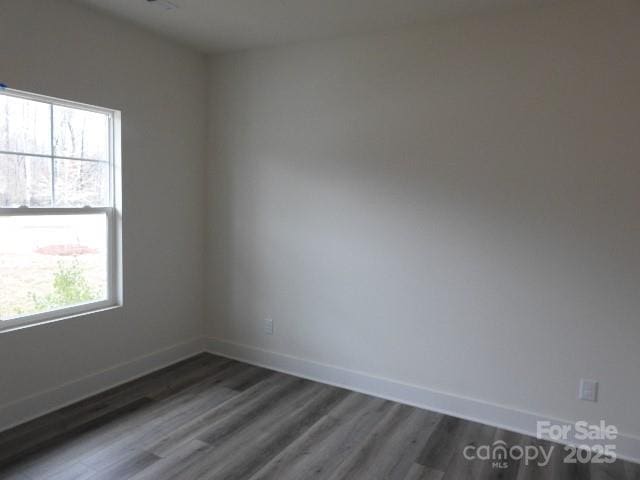 empty room featuring dark wood finished floors, plenty of natural light, and baseboards