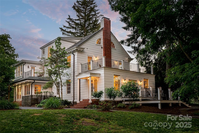 view of front of house featuring a chimney, a lawn, and a balcony