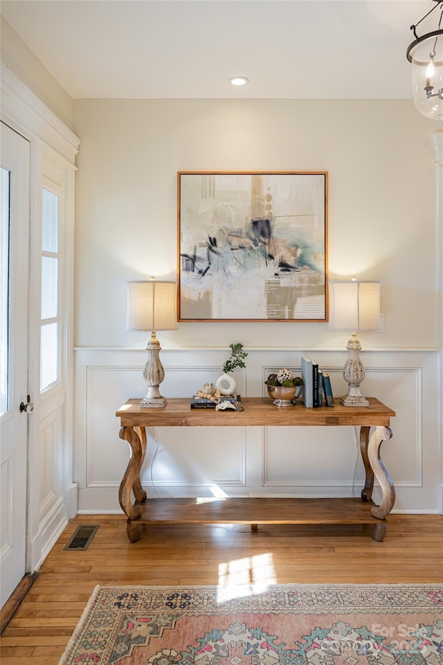 entrance foyer with a decorative wall, a notable chandelier, wood finished floors, visible vents, and wainscoting