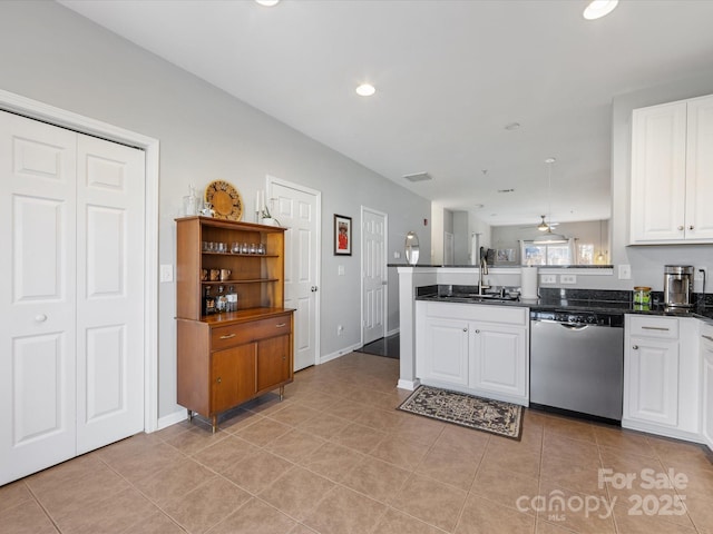 kitchen featuring dark countertops, stainless steel dishwasher, white cabinets, a sink, and a peninsula