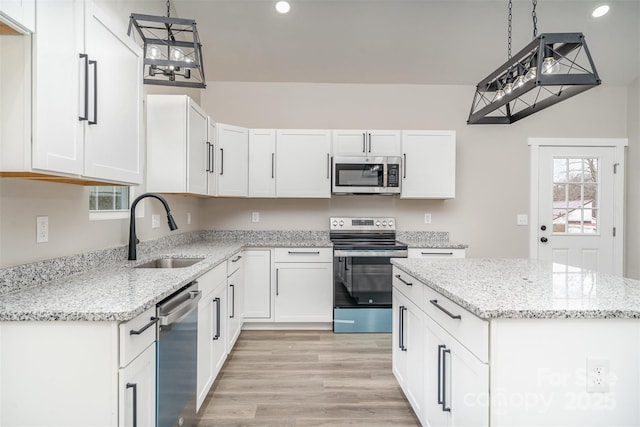 kitchen with light wood-style flooring, stainless steel appliances, a sink, white cabinetry, and a center island