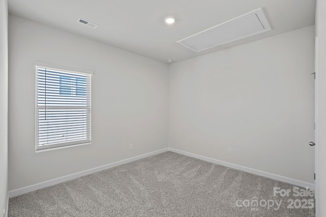 carpeted spare room with visible vents, baseboards, and attic access