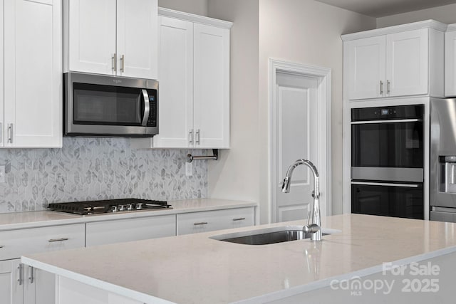 kitchen with light stone counters, a sink, white cabinetry, appliances with stainless steel finishes, and tasteful backsplash