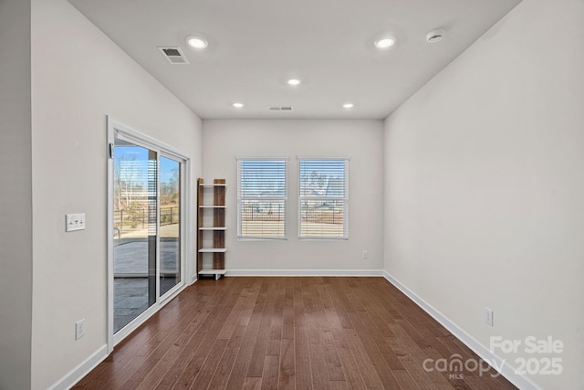 spare room with dark wood-style flooring, visible vents, and baseboards