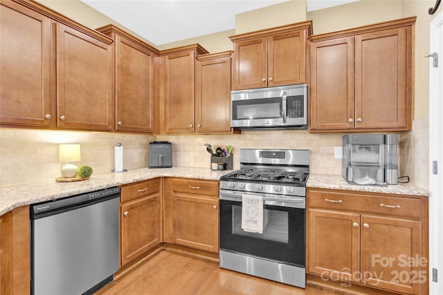 kitchen with appliances with stainless steel finishes, backsplash, light wood-style flooring, and light stone counters